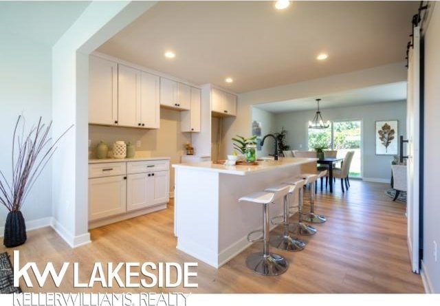 kitchen featuring pendant lighting, white cabinetry, light wood-type flooring, a center island with sink, and an inviting chandelier