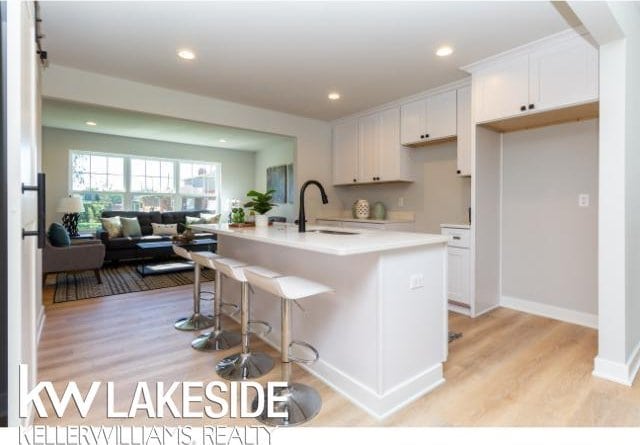 kitchen with white cabinetry, light hardwood / wood-style floors, a kitchen island with sink, and sink