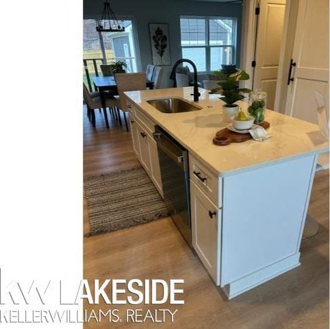 kitchen with pendant lighting, white cabinetry, sink, black dishwasher, and a kitchen island with sink