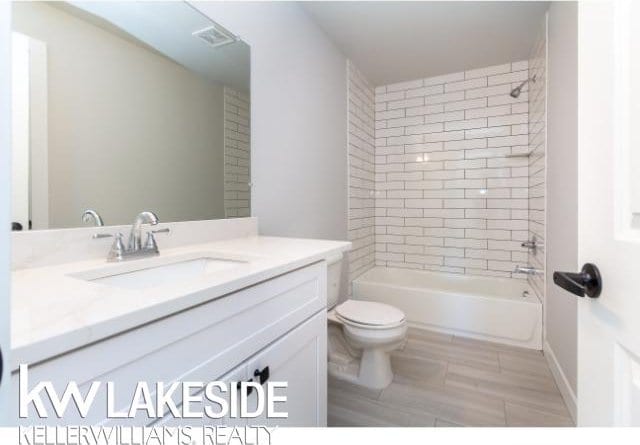 full bathroom with tiled shower / bath, vanity, and toilet