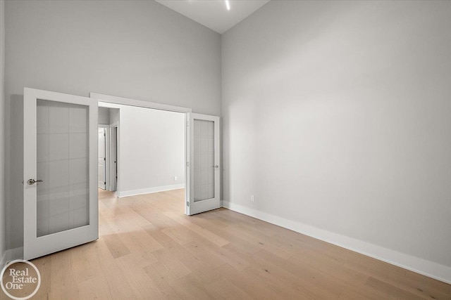 unfurnished bedroom featuring french doors, a towering ceiling, and light hardwood / wood-style floors