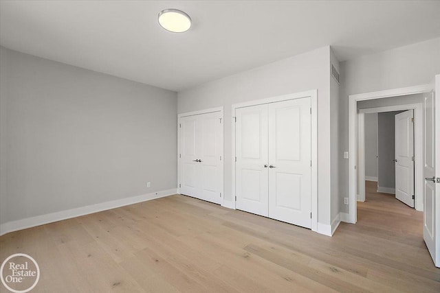 unfurnished bedroom with light hardwood / wood-style flooring and multiple closets