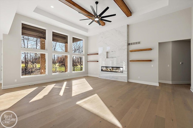 unfurnished living room with ceiling fan, a fireplace, a towering ceiling, and hardwood / wood-style flooring