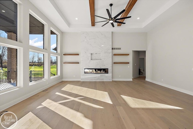 unfurnished living room featuring a premium fireplace, ceiling fan, a high ceiling, and light wood-type flooring