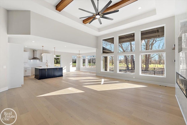 unfurnished living room with sink, a high ceiling, light hardwood / wood-style floors, a tiled fireplace, and ceiling fan with notable chandelier