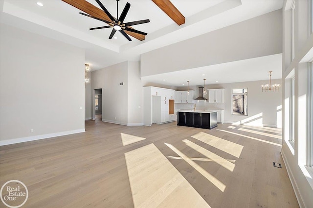 unfurnished living room featuring beam ceiling, a high ceiling, light hardwood / wood-style floors, and ceiling fan with notable chandelier