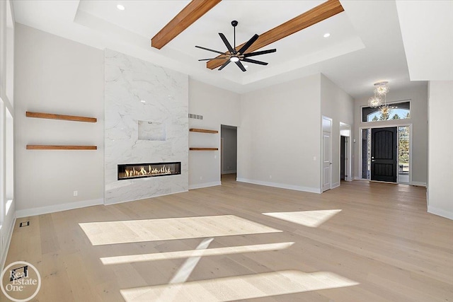 unfurnished living room featuring ceiling fan, a raised ceiling, a premium fireplace, a towering ceiling, and light wood-type flooring