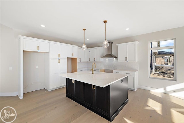 kitchen with a center island with sink, white cabinets, wall chimney range hood, sink, and light wood-type flooring