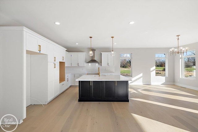 kitchen with a wealth of natural light, light hardwood / wood-style flooring, a kitchen island with sink, and wall chimney range hood