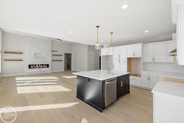 kitchen with dishwasher, light hardwood / wood-style flooring, an island with sink, a fireplace, and white cabinets