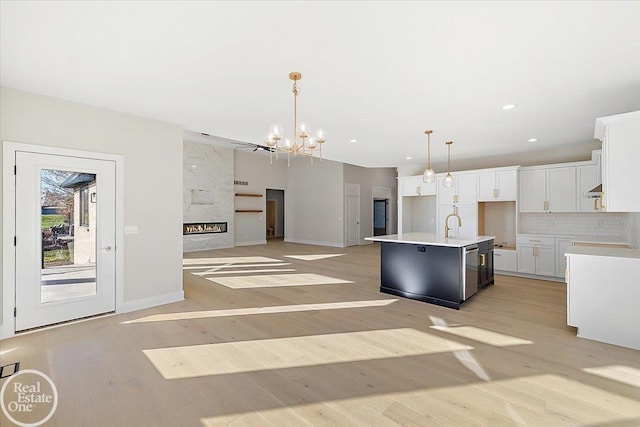 kitchen with pendant lighting, a center island with sink, light hardwood / wood-style flooring, a premium fireplace, and white cabinets