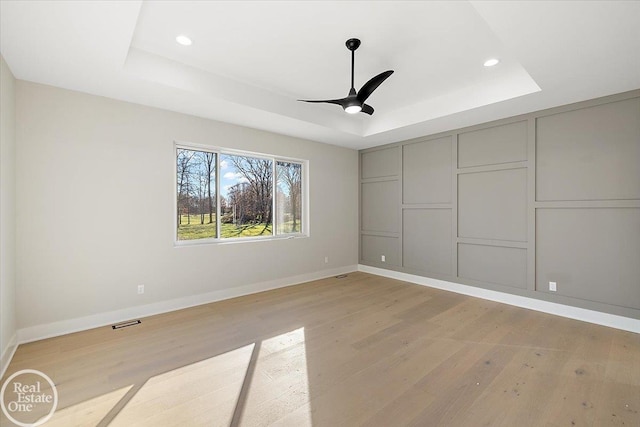 spare room with a tray ceiling, ceiling fan, and light hardwood / wood-style flooring