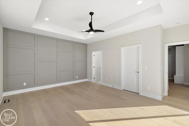 unfurnished bedroom with ceiling fan, light hardwood / wood-style flooring, and a tray ceiling