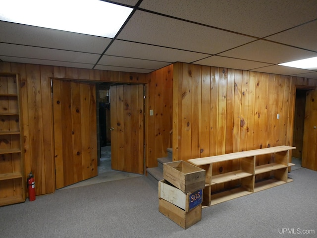 basement with carpet flooring, a drop ceiling, and wooden walls