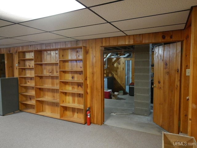 basement with wood walls, a drop ceiling, and light colored carpet