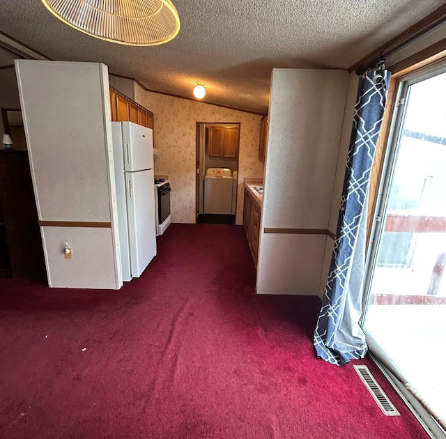 kitchen featuring a textured ceiling, white appliances, vaulted ceiling, washer and clothes dryer, and dark colored carpet