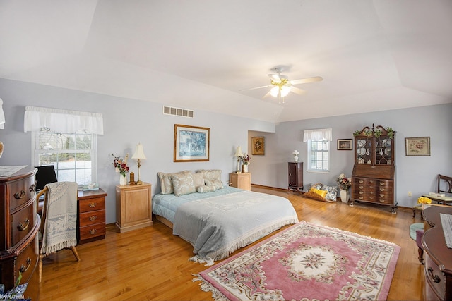 bedroom with a raised ceiling, multiple windows, ceiling fan, and light hardwood / wood-style floors