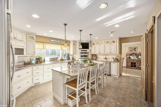 kitchen with light stone countertops, a kitchen breakfast bar, tasteful backsplash, decorative light fixtures, and a center island