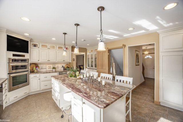 kitchen with dark stone counters, double oven, a kitchen island, a kitchen bar, and white cabinetry