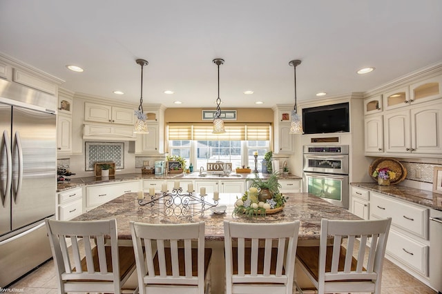 kitchen with appliances with stainless steel finishes, a center island, pendant lighting, and dark stone countertops