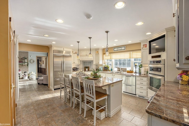 kitchen featuring dark stone counters, hanging light fixtures, appliances with stainless steel finishes, a kitchen island, and a breakfast bar area