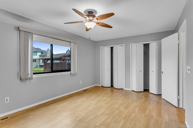 unfurnished bedroom with ceiling fan, light wood-type flooring, and multiple closets