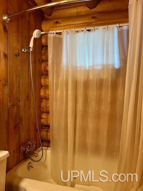 bathroom with log walls and shower / bath combo