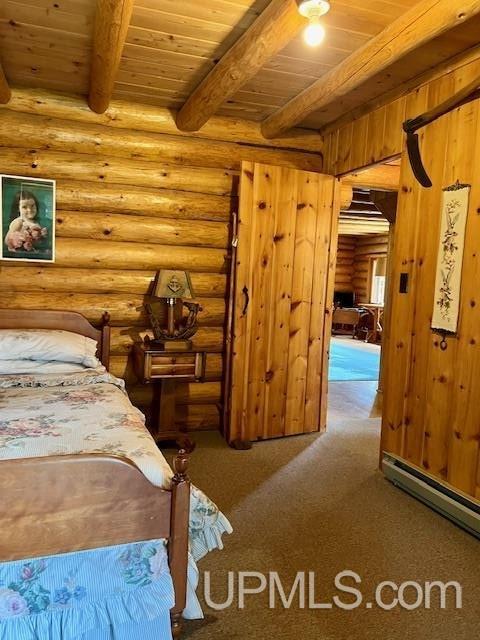 carpeted bedroom with beam ceiling, rustic walls, baseboard heating, and wood ceiling