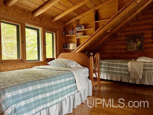 bedroom featuring hardwood / wood-style floors, lofted ceiling with beams, rustic walls, and wood ceiling