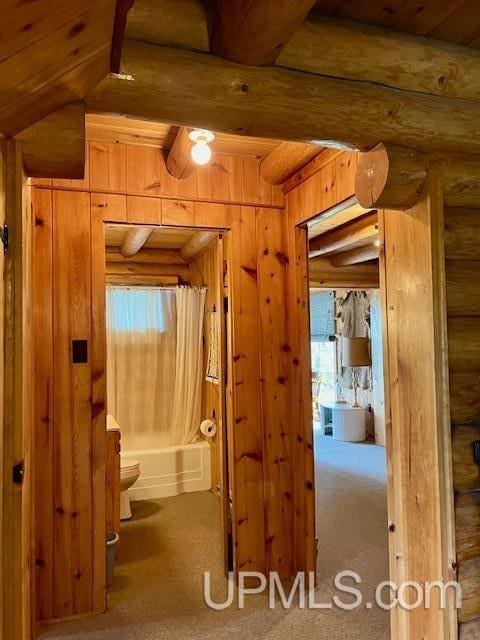 hall featuring wooden walls, lofted ceiling with beams, carpet floors, and a wealth of natural light