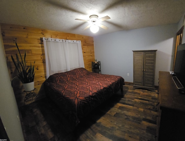 bedroom with wood walls, ceiling fan, dark wood-type flooring, and a textured ceiling