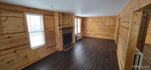 unfurnished living room featuring radiator heating unit, dark hardwood / wood-style floors, and wood walls