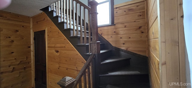 stairway with a textured ceiling and wood walls