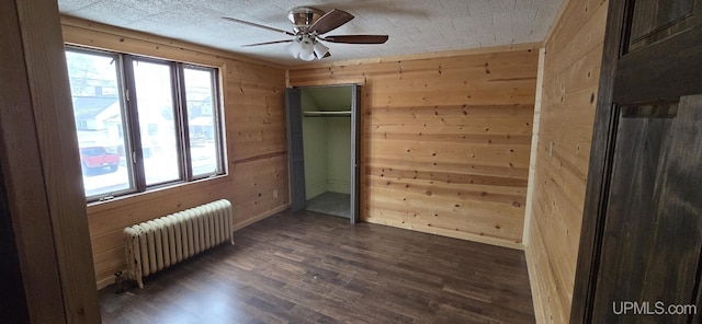 spare room featuring dark hardwood / wood-style floors, ceiling fan, radiator heating unit, and wooden walls