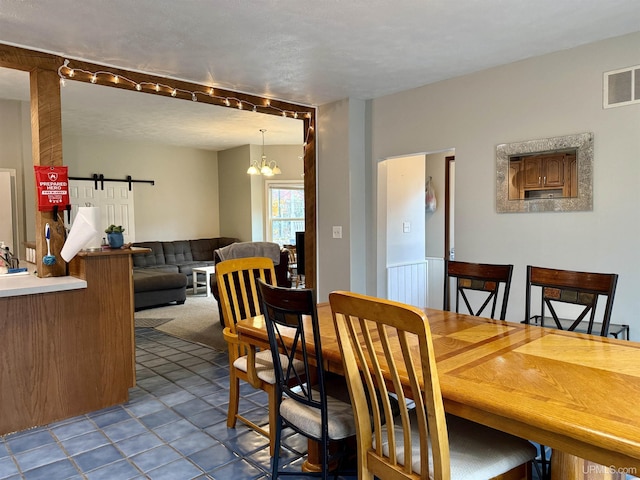 carpeted dining area with a barn door, a textured ceiling, and a notable chandelier