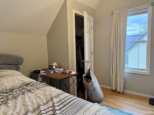 bedroom with a textured ceiling, light wood-type flooring, and lofted ceiling