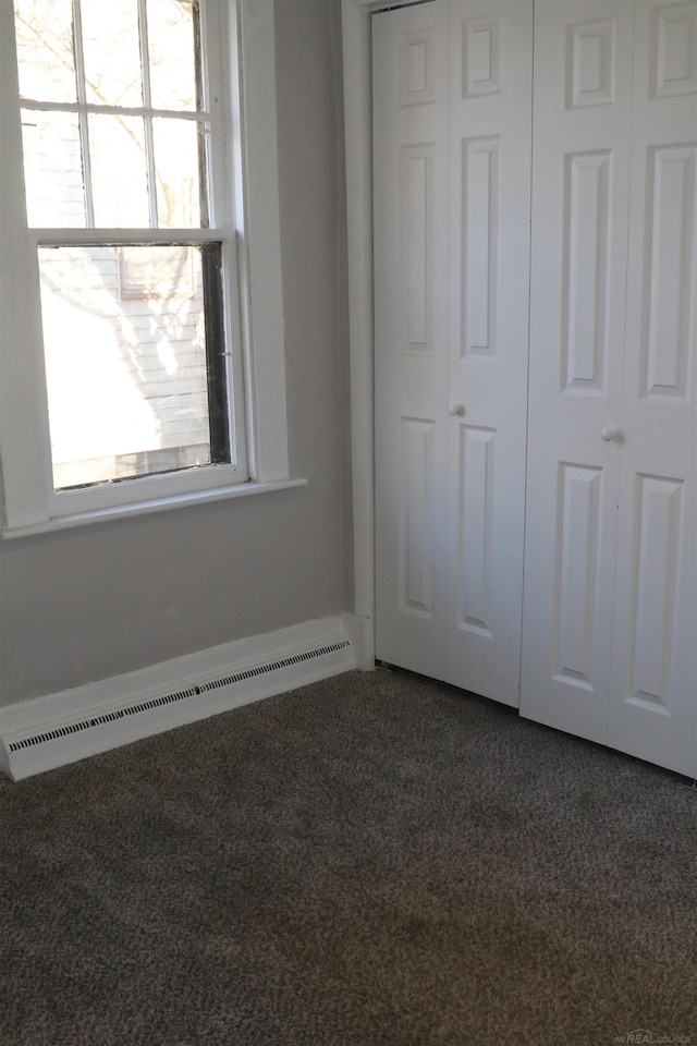 unfurnished bedroom with a closet, a baseboard radiator, and dark carpet