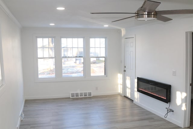 unfurnished living room with light wood-type flooring, a wealth of natural light, and crown molding