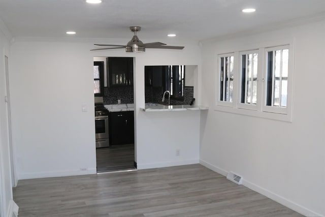 kitchen with ceiling fan, backsplash, crown molding, stainless steel stove, and light wood-type flooring