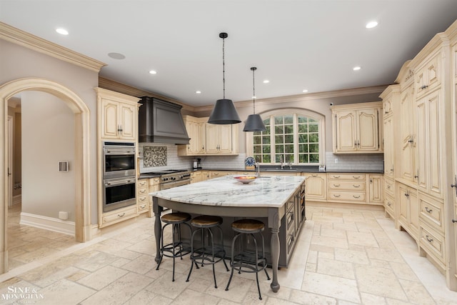 kitchen featuring decorative backsplash, custom range hood, a center island with sink, and light stone countertops