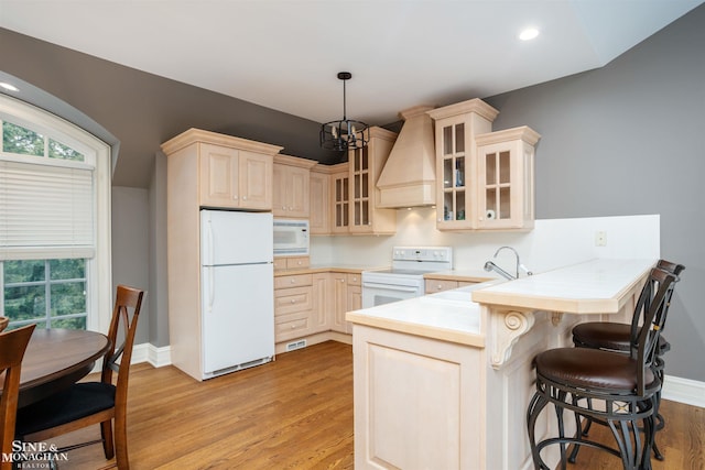 kitchen featuring custom exhaust hood, light hardwood / wood-style floors, white appliances, and a chandelier