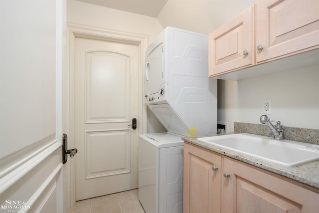 clothes washing area featuring stacked washer / dryer, sink, light tile patterned floors, and cabinets