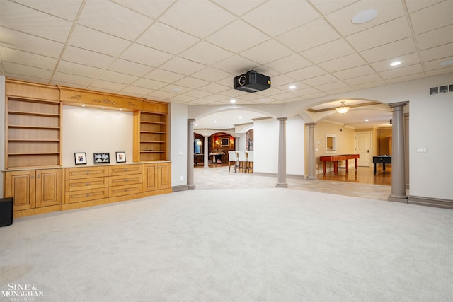 basement with a paneled ceiling, built in shelves, and light carpet