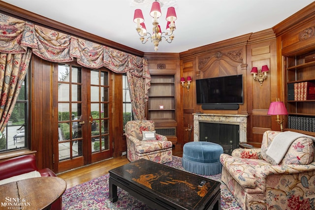 living room with an inviting chandelier, french doors, crown molding, light hardwood / wood-style flooring, and built in shelves