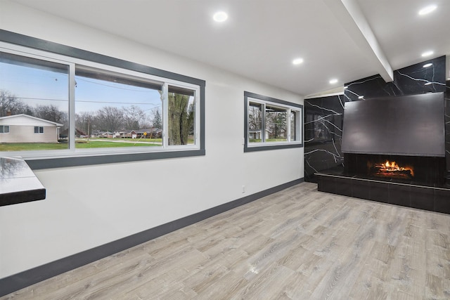 unfurnished living room featuring beamed ceiling, light hardwood / wood-style floors, and a tile fireplace