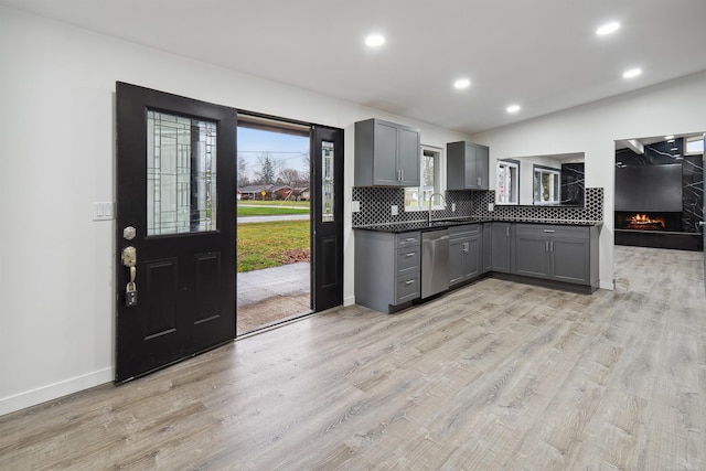 kitchen featuring sink, stainless steel dishwasher, gray cabinets, decorative backsplash, and light wood-type flooring