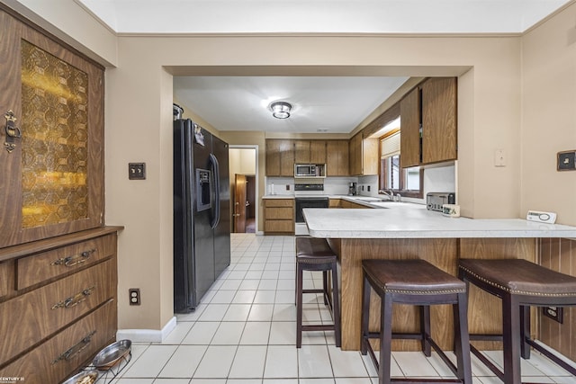 kitchen featuring kitchen peninsula, black fridge, electric stove, stainless steel microwave, and light tile patterned flooring