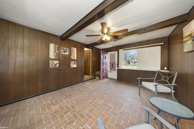 interior space featuring beam ceiling, ceiling fan, and wood walls