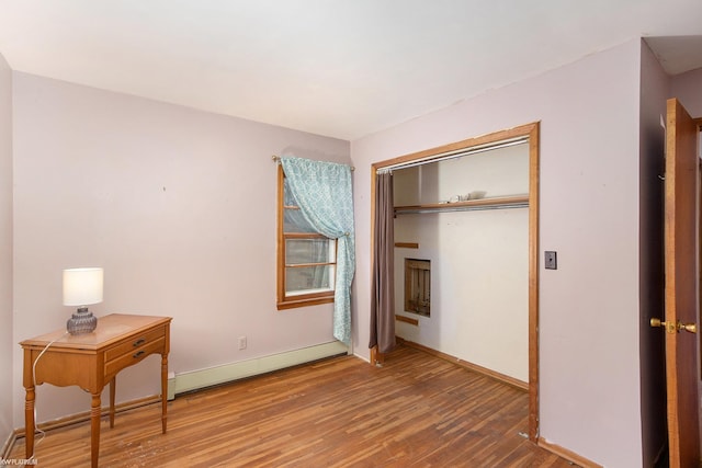 bedroom with wood-type flooring, baseboard heating, and a closet