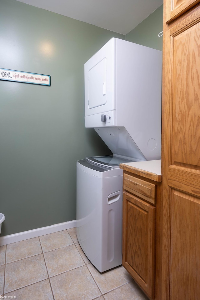 clothes washing area with cabinets, stacked washing maching and dryer, and light tile patterned floors